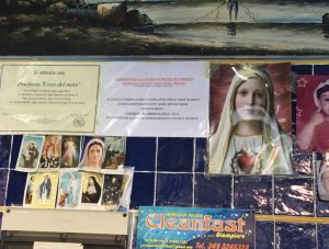いつも行くお魚屋さん。壁にマリア様や聖人のブロマイド的なものが店の営業許可証や自分の子供の写真と一緒にペタペタ貼ってあります